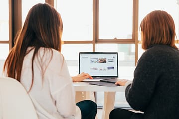 Duas mulheres vendo uma landing page na tela do computador.
